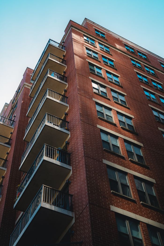 about-us A tall brick apartment building with balconies in urban sunlight.