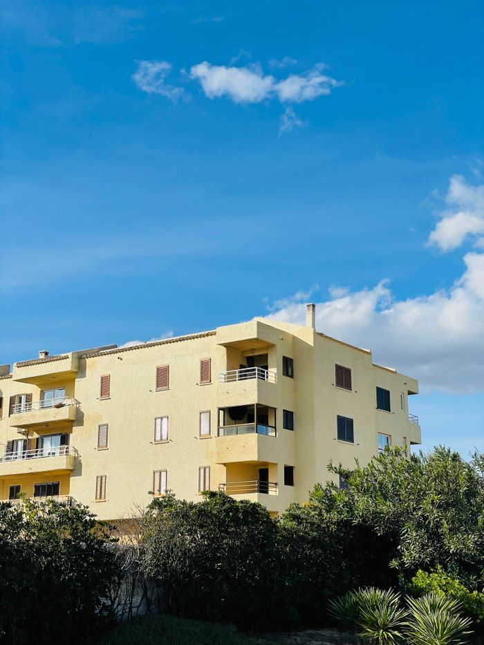 Sunny apartment building with lush greenery against a blue sky.