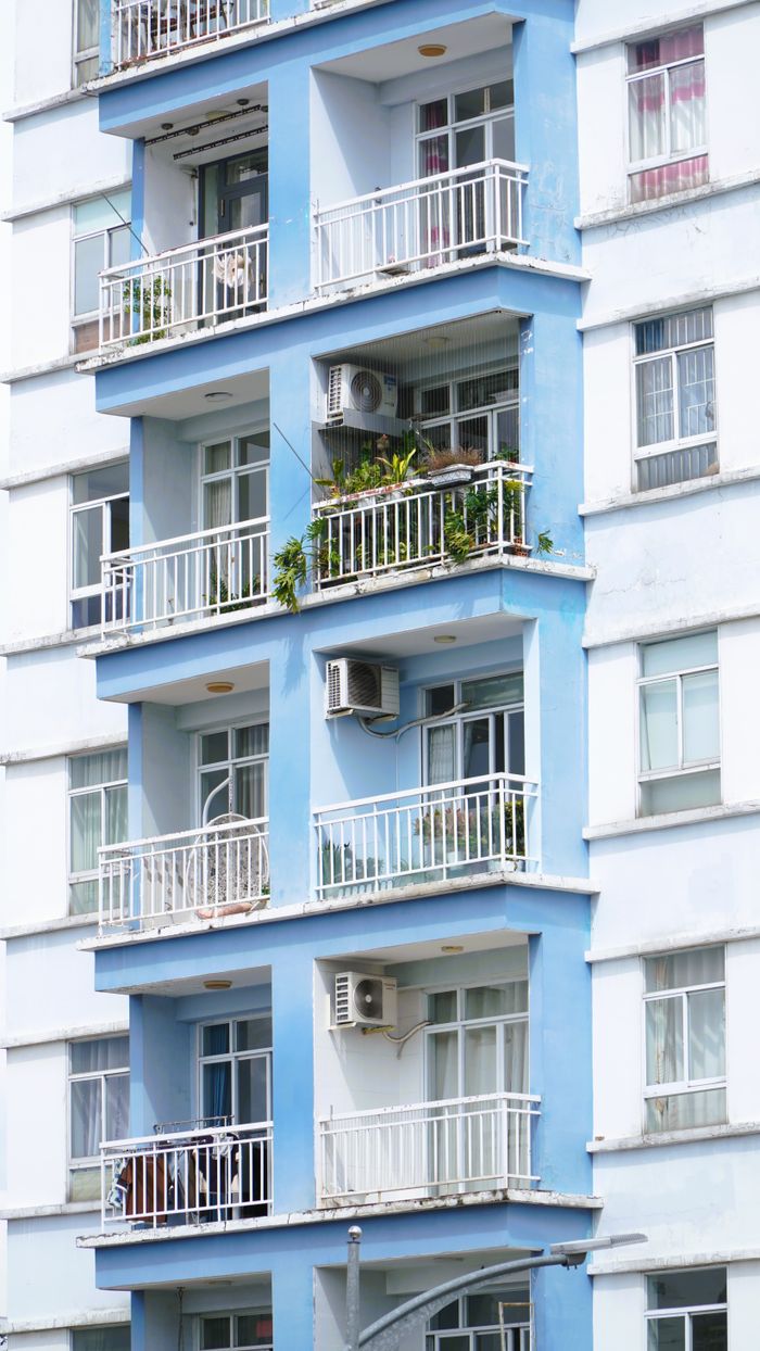 Close-up view of a modern apartment building with balconies and air conditioners, featuring blue accents.